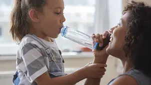 Smiling parent helping their child use an inhaler with a spacer 